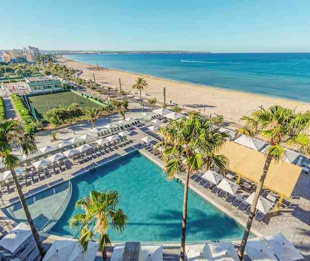 Udsigt over en pool med solsenge og parasoller ved en strand i et bymiljø. (AI-genereret tekst)