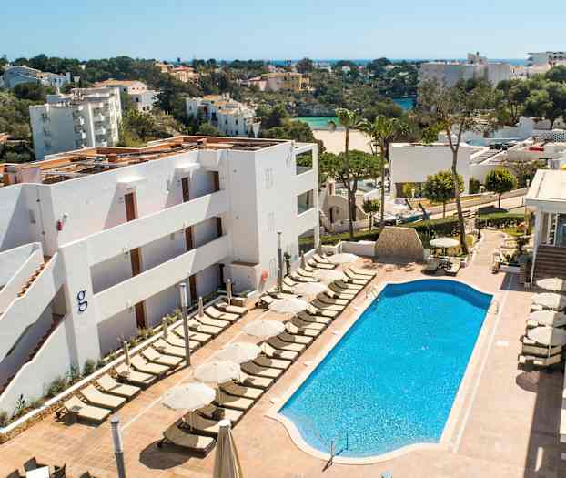 Billede af et hotelområde med en swimmingpool og liggestole. I baggrunden ses grønne områder og bygninger. (AI-genereret tekst)