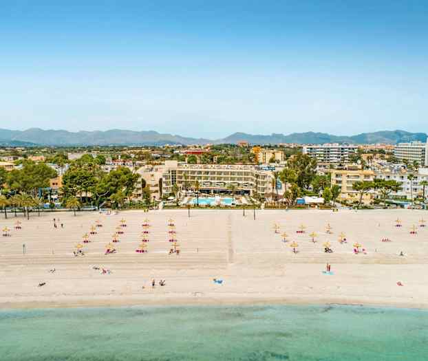 Strand med liggestole og parasoller, hoteller samt bysilhuet i baggrunden. (AI-genereret tekst)