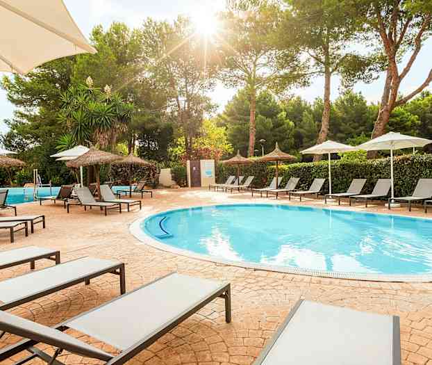 Solstole ved en pool med parasoller og træer i baggrunden. (AI-genereret tekst)