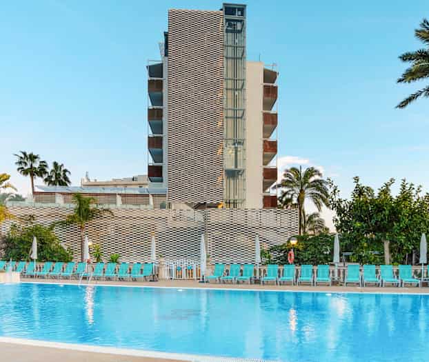 En bygning med en pool foran samt palmer og solvogne. (AI-genereret tekst)