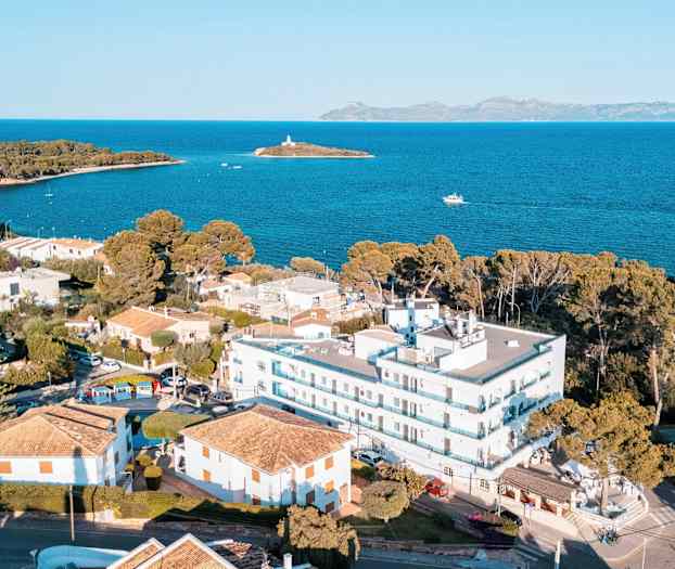 Luftfoto af et kystområde med bygninger, strandnære huse og havudsigt med en lille ø i baggrunden. (AI-genereret tekst)