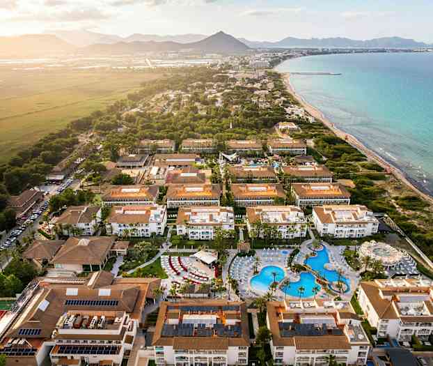 Luftfoto af et turistområde med hoteller og swimmingpool ved kysten. (AI-genereret tekst)