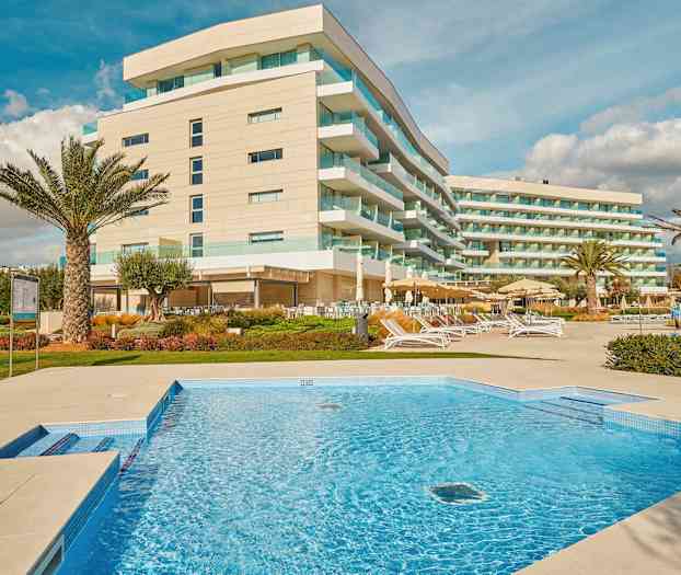 Billede af et hotel med moderne bygninger, en swimmingpool og udendørs loungeområder. (AI-genereret tekst)