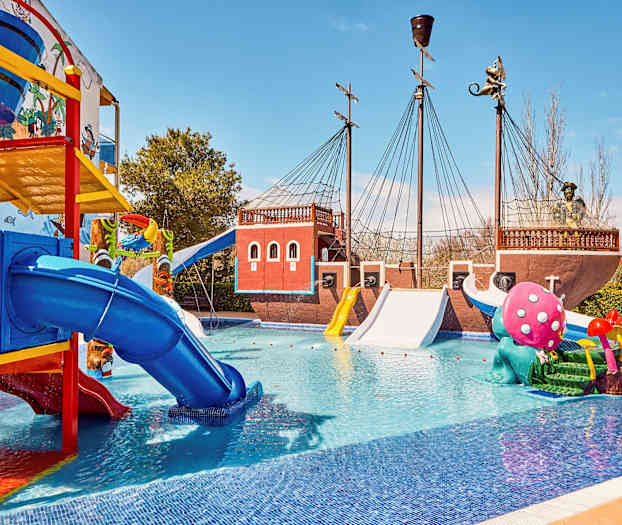 Billede af en vandpark med et pirattematisk skib, farverige rutsjebaner og legeskulpturer i en pool. (AI-genereret tekst)