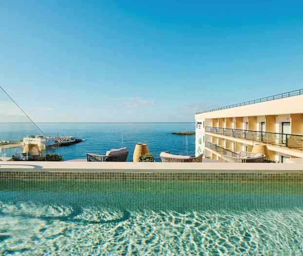 Udendørs pool med udsigt over havet og en hotelbygning. (AI-genereret tekst)