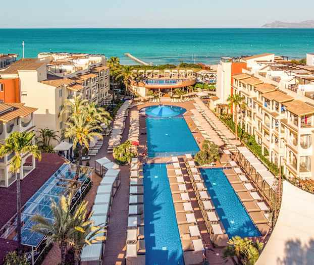 Udsigt over en resort med swimmingpools og havet i baggrunden. (AI-genereret tekst)