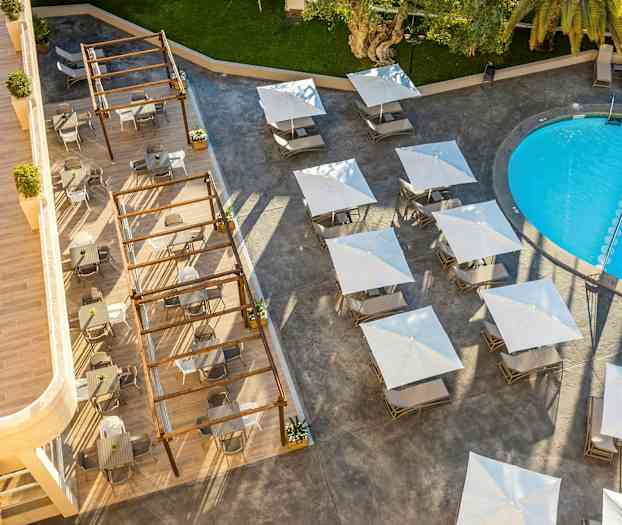 Udsigt fra oven over en udendørs pool, borde med parasoller og siddepladser. (AI-genereret tekst)