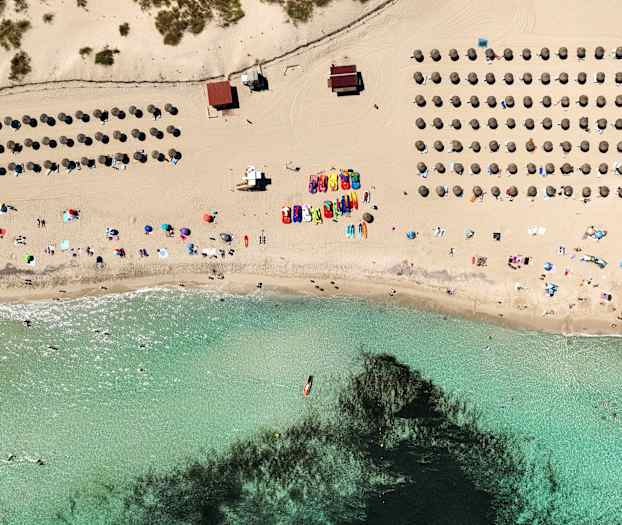 Luftfoto af en strand med parasoller, mennesker og klart vand. (AI-genereret tekst)