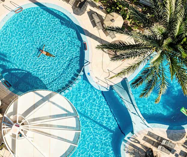 En udendørs pool omgivet af solsenge og parasoller, med en person der svømmer. (AI-genereret tekst)