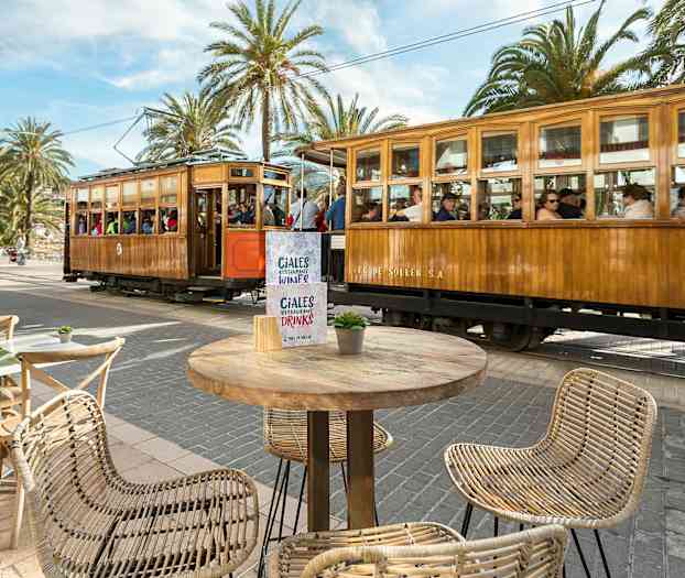 En sporvogn af træ passerer ved et torv med borde og stole. (AI-genereret tekst)