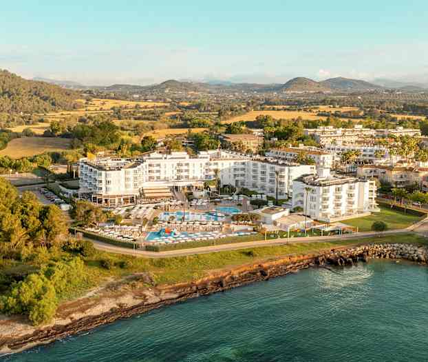 Luftfoto af et hotelkompleks omgivet af grønne områder og vandet. (AI-genereret tekst)