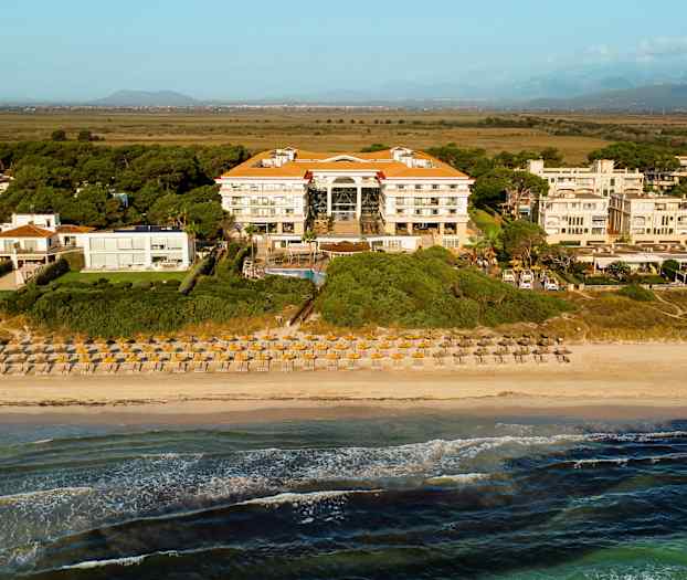 Udsigt over en strand med liggestole og parasoller foran et hotel omgivet af bevoksning. (AI-genereret tekst)