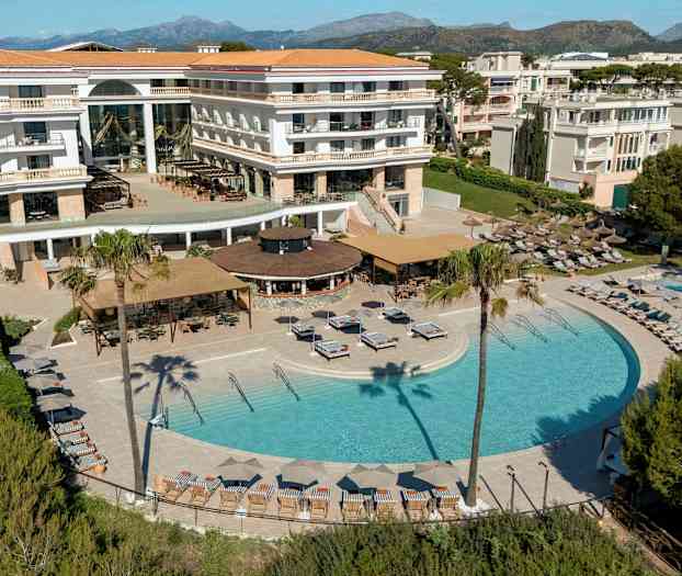 Hotel med pool- og terrasseområde omgivet af liggestole, parasoller og grønt. (AI-genereret tekst)