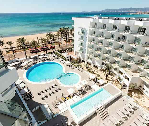 Hotelområde med pool og liggestole, strand og hav i baggrunden. (AI-genereret tekst)