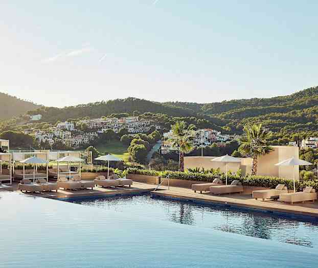 En udsigt fra et hotelområde med en pool omgivet af liggestole, parasoller og et frodigt landskab i baggrunden. (AI-genereret tekst)