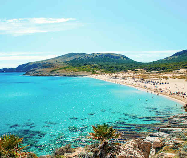 En sandstrand med turkisblåt vand og grønne bakker i baggrunden. (AI-genereret tekst)