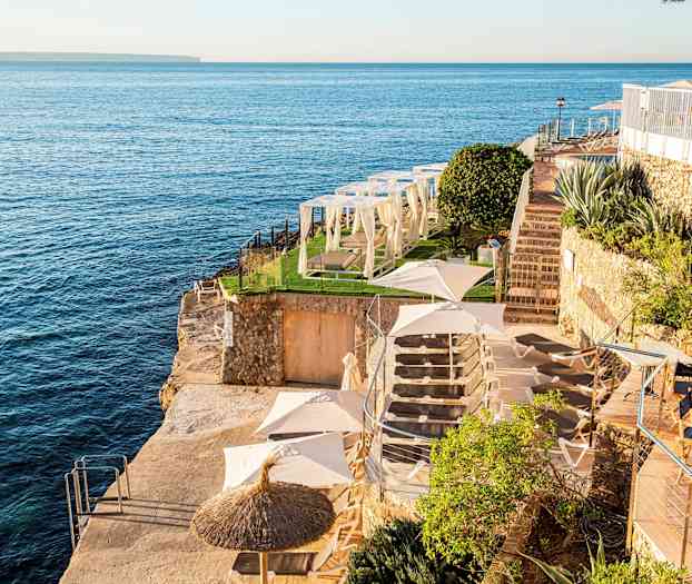 Udsigt over en klippeafsat ved havet med liggestole, parasoller og grønne områder. (AI-genereret tekst)