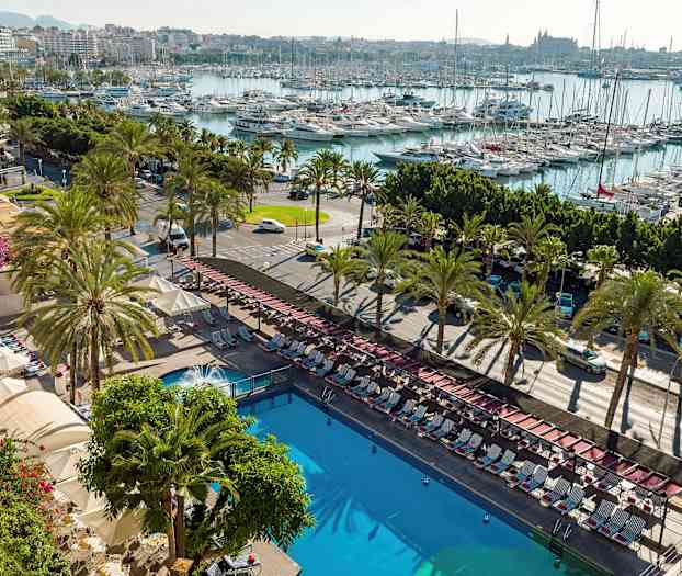 Udsigt over en udendørs pool omgivet af liggestole og parasoller, med en vej omkranset af palmer og en marina fyldt med både i baggrunden. (AI-genereret tekst)