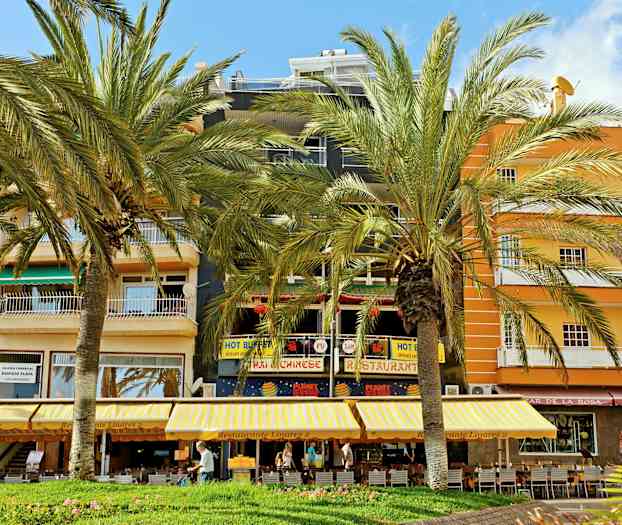 En bygning med restauranter og butikker samt palmer foran. (AI-genereret tekst)