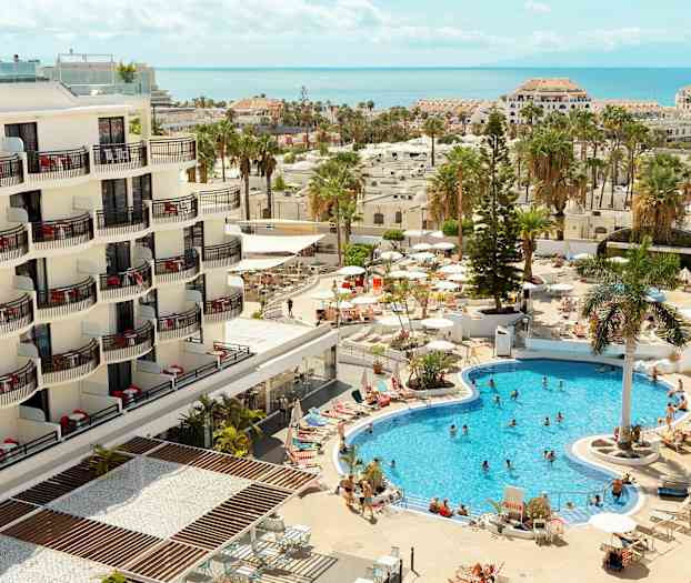 Et hotel med altaner og et poolområde med gæster og parasoller. (AI-genereret tekst)