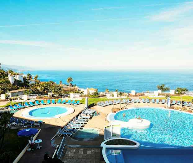 Billede af et hotel med poolområde i forgrunden og havudsigt i baggrunden. (AI-genereret tekst)