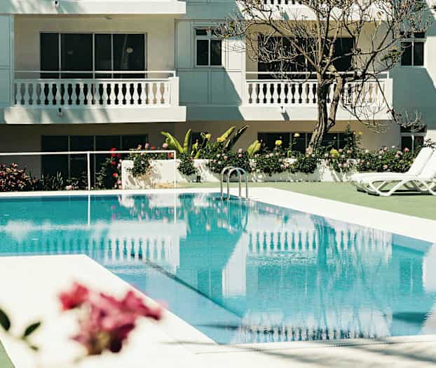 Udendørs swimmingpool med liggestole ved et hvidmalet hotel. (AI-genereret tekst)