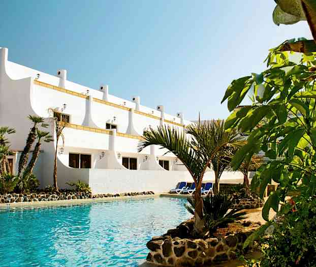 Hvid bygning med palmer ved en pool. (AI-genereret tekst)