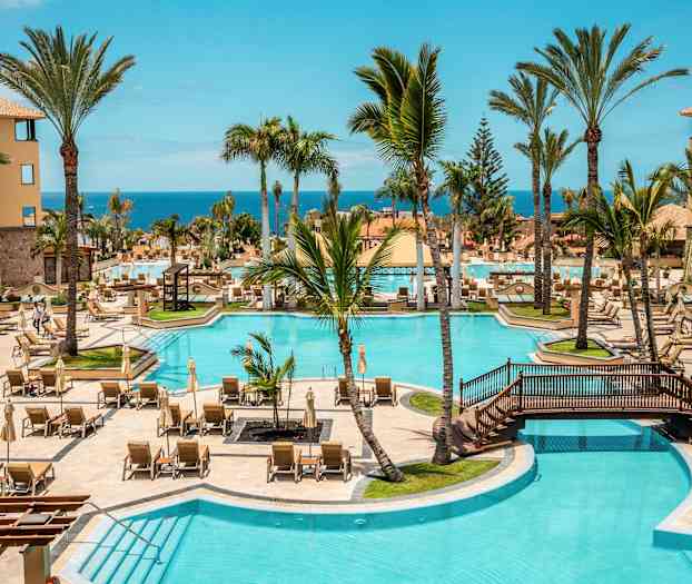 Hotel poolområde med liggestole, palmer og udsigt til havet. (AI-genereret tekst)