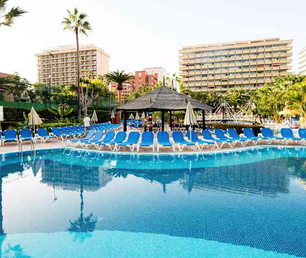 En pool med liggestole omkring og hotelbygninger i baggrunden. (AI-genereret tekst)