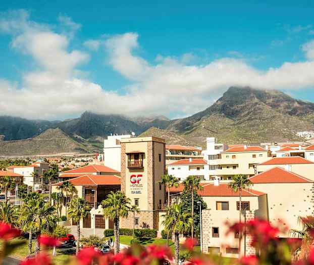 Udsigt over hotelområdet med bjerge i baggrunden under en blå himmel. (AI-genereret tekst)