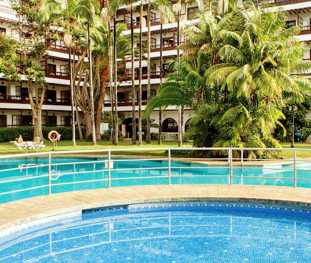 Udendørs swimmingpool foran en hotelbygning med altaner og frodige træer. (AI-genereret tekst)