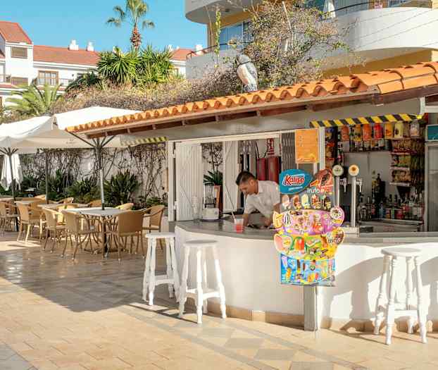 En udendørs terrasse med borde og parasoller ved siden af en bar. (AI-genereret tekst)