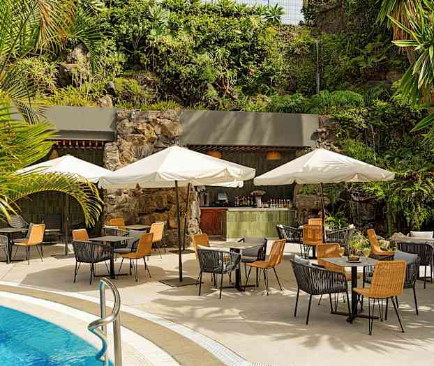 Udendørs servering ved poolen med borde, stole og parasoller. Baggrunden har grøn vegetation og en mindre bar. (AI-genereret tekst)