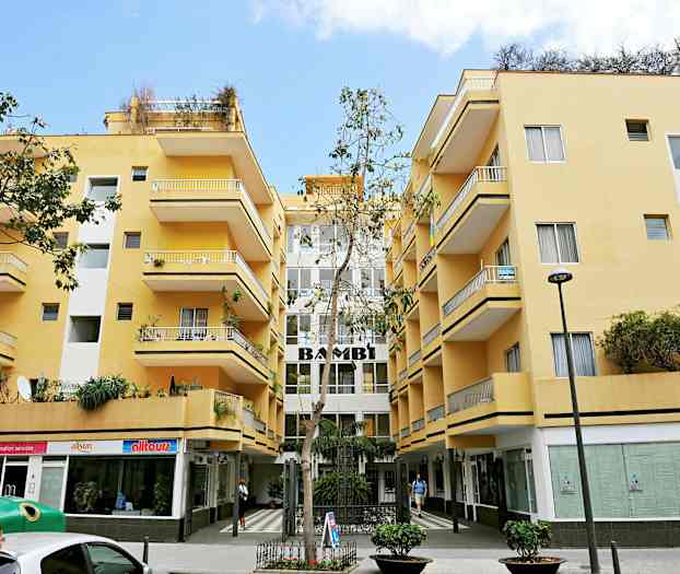 Gul bygning med altaner og butikker i stueetagen. (AI-genereret tekst)