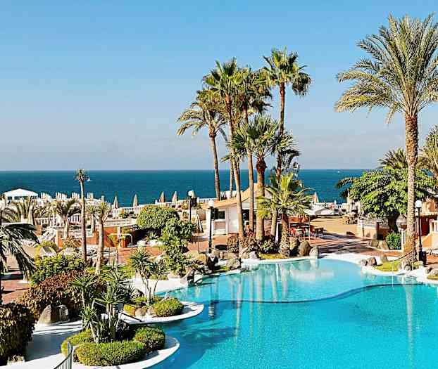 Et feriested med en pool, omgivet af palmer og med udsigt over havet i baggrunden. (AI-genereret tekst)