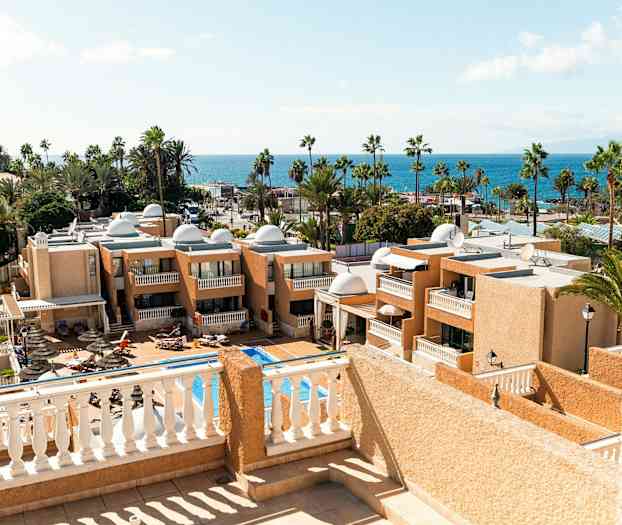 Udsigt over hotelbygninger og en pool med havet i baggrunden. (AI-genereret tekst)