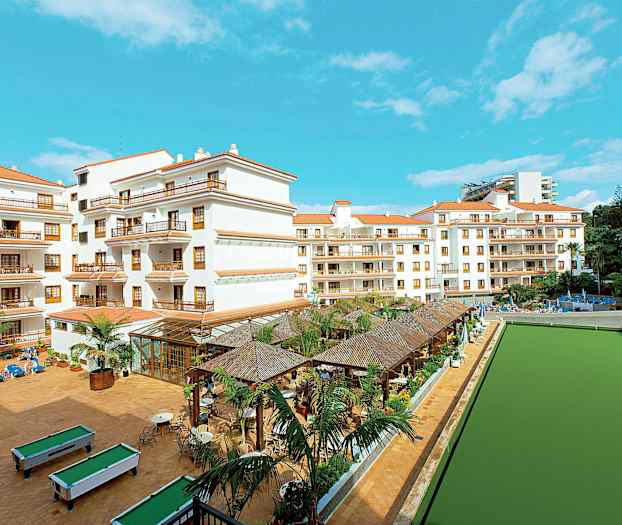 Flere hvidmalede bygninger med røde tage omgivet af en stor gårdhave med pool og siddepladser. (AI-genereret tekst)