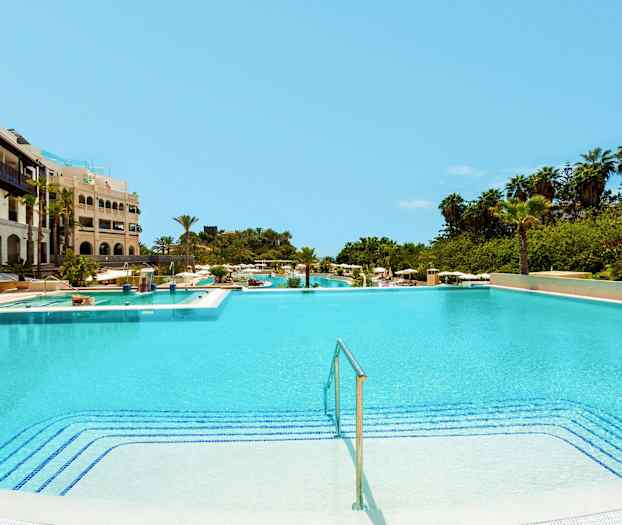 Stor swimmingpool ved et hotel med omgivende grønne områder. (AI-genereret tekst)