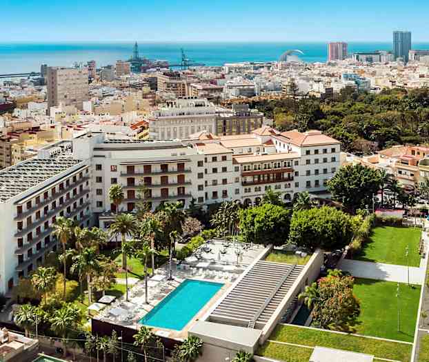 Udsigt over bymiljø med bygninger, grønne områder og pool. (AI-genereret tekst)