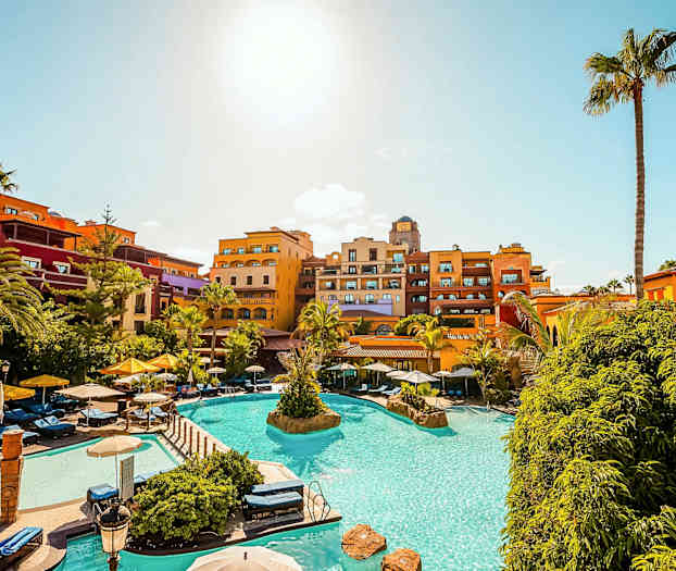 Ferieanlæg med pool, liggestole og farverige hotelbygninger under en klar blå himmel. (AI-genereret tekst)