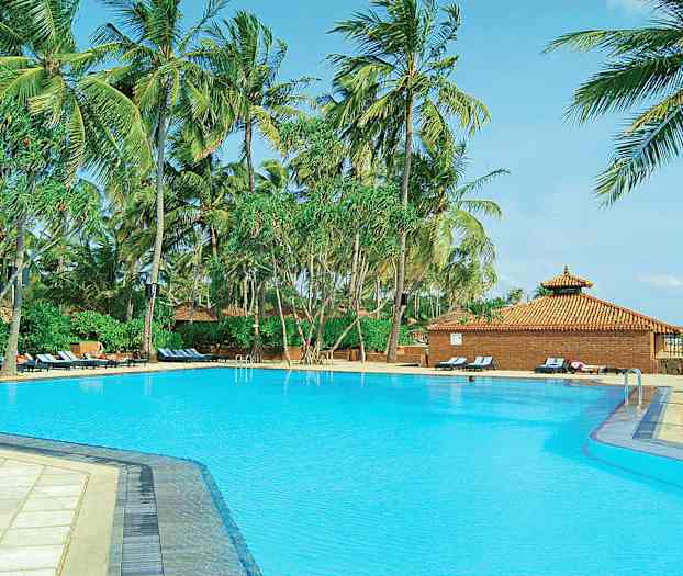 En stor pool omgivet af høje palmer og liggestole tæt på en bygning med tegltag. (AI-genereret tekst)