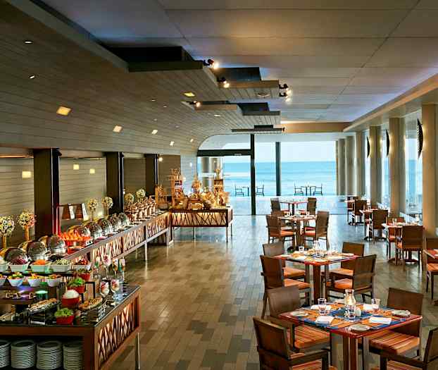 Billede af en restaurant med opdækkede borde og en buffet med forskellige retter samt store vinduer med udsigt til havet. (AI-genereret tekst)