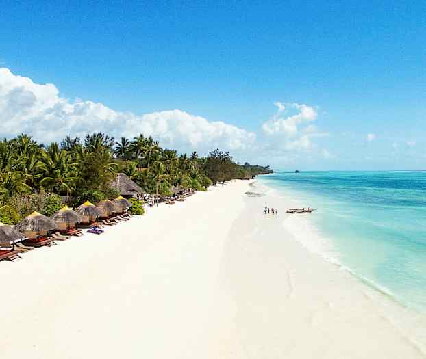 En strand med hvid sand og klart blåt vand, omgivet af frodige palmer og parasolstole. (AI-genereret tekst)