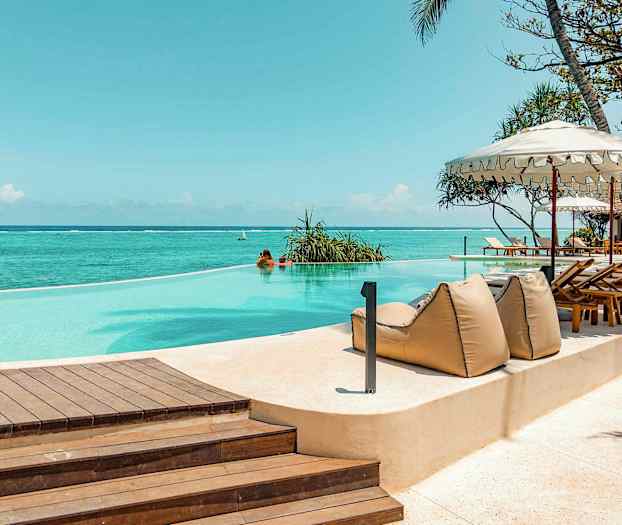 En infinity-pool ved havet, omgivet af liggestole og parasoller. (AI-genereret tekst)