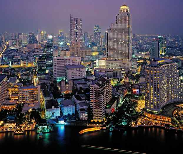 En byscene om aftenen oplyst af bygninger og gadebelysning, med en flod i forgrunden. (AI-genereret tekst)