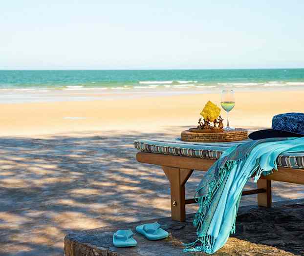 Liggestol med en hat, håndklæde og klipklapper ved stranden. (AI-genereret tekst)