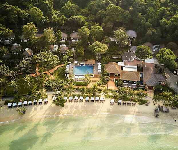 Luftfoto af en ferieresort ved stranden med palmer, liggestole og en pool, omgivet af frodigt grønt. (AI-genereret tekst)