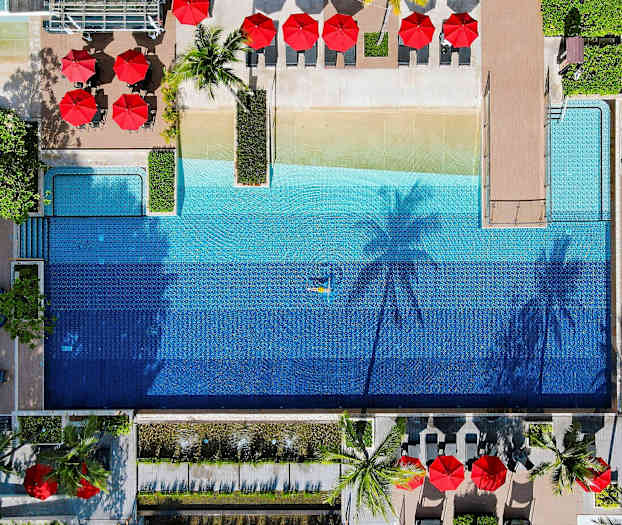 Luftfoto af en udendørs pool omgivet af liggestole og parasoller. (AI-genereret tekst)