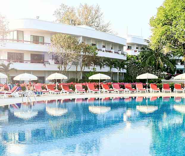 Poolområde med liggestole og parasoller foran et hotel. (AI-genereret tekst)